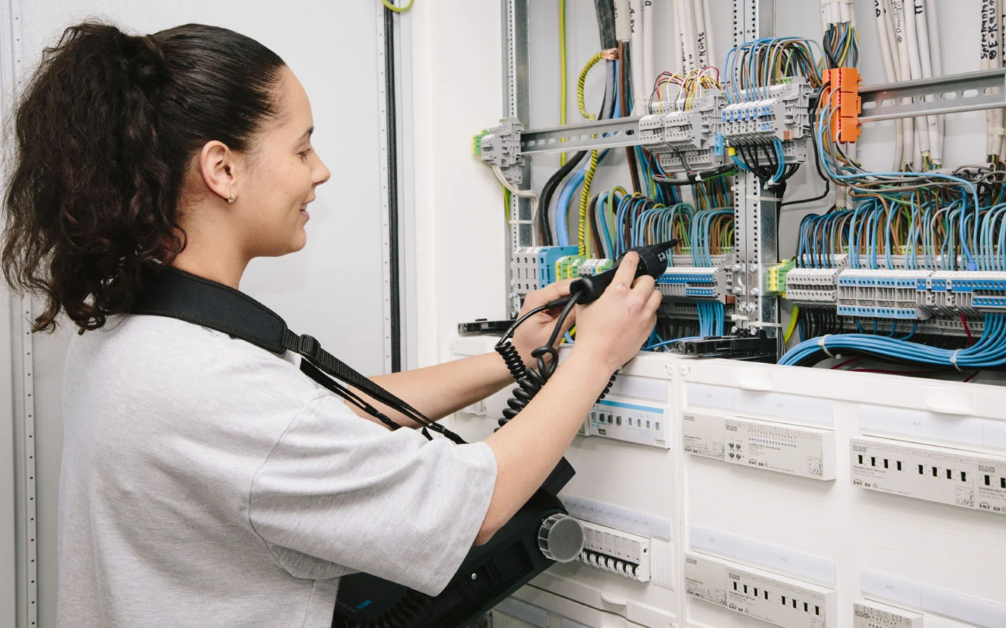 E-CHECK - Mitarbeiterin prüft im Schaltschrank mit einem Meßgerät &middot; ABE Elektrotechnik